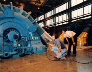 Photo is engineers Michael Bishop and Scott Burgess posed in front of a large power turbine